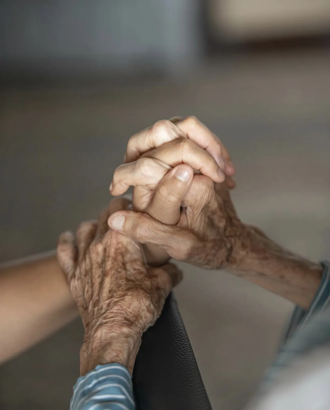 Manos de una abuela sostenidas con cariño por las manos de una cuidadora